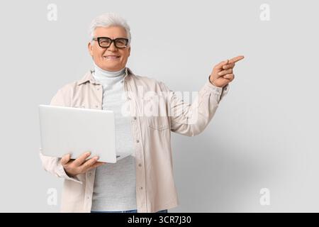 Senior programmer with laptop pointing at something on light background Stock Photo