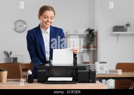 Young businesswoman with modern printer and ink on table in office Stock Photo