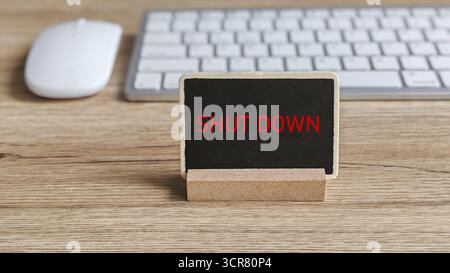 Red SHUT DOWN Text on Chalkboard Sign on Wooden Desk with Computer Mouse and Keyboard in Background Stock Photo