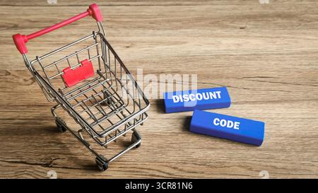 Discount Code or Coupon Concept: Miniature Shopping Cart and Blue Blocks with White Text on a Wood Table. Stock Photo