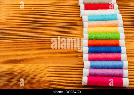 A collection of vibrant thread spools displayed neatly on a rustic wooden surface, showcasing various colors ideal for sewing and crafting activities. Stock Photo