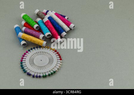 Brightly colored spools of thread are arranged alongside a circular holder filled with vibrant pins, creating an inviting atmosphere for crafting and Stock Photo