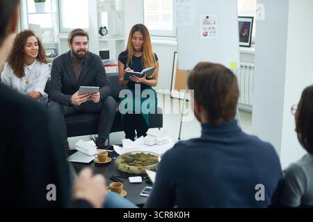 Architects and designers at conference. Young male and female specialists discussing design of new townhouses while sitting in modern office. Foam board house models placed on table in front of them. Stock Photo