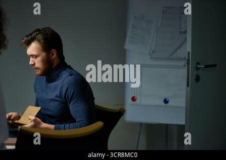 Working in construction company. Bearded businessman in turtleneck sitting at desk in office and using digital tablet Stock Photo