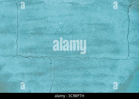 Surface of a turquoise wall displaying cracks and a rough texture under bright sunlight, adding visual interest to the setting. Stock Photo