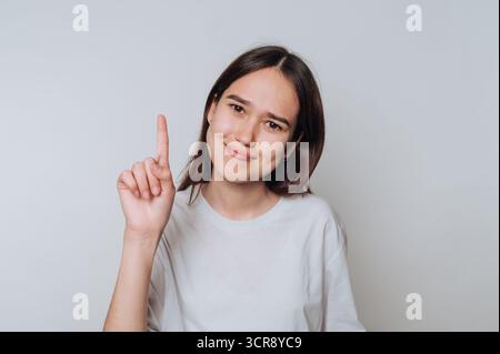 Woman showing a finger gesture to indicate a thoughtful idea while wearing a casual shirt in a bright indoor setting Stock Photo