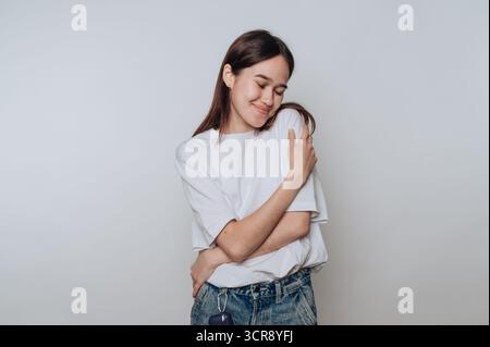 Woman embracing herself with a warm smile in a simple indoor setting Stock Photo