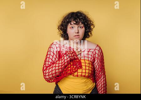 Young person expressing surprise in a vibrant yellow setting with a unique layered outfit Stock Photo