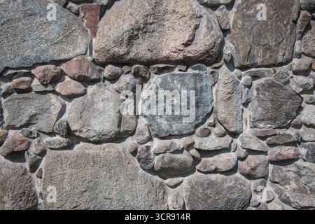 A wall made of large rocks with a grayish color. The wall is made of many different sized rocks, and it is a part of a building. The wall has a rough Stock Photo