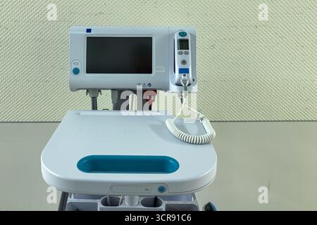 A sleek medical monitoring device sits on a clean surface, displaying information for patient care. It features a screen, buttons, and a coiled cord, ready for use in a clinical environment. Stock Photo