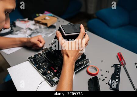 Close-up of computer technician installing CPU cooler on motherboard, working in dimly lit workshop with scattered computer components Stock Photo