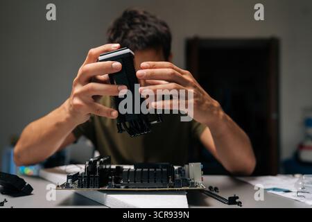 Front view of computer technician installing CPU cooler onto motherboard, performing maintenance and repair work on desktop computer in dark workshop Stock Photo