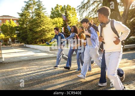 Group of diverse university students with backpacks running across campus at golden hour, laughing and celebrating friendship, energy, youth and futur Stock Photo
