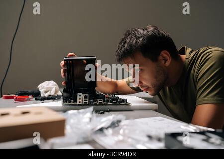 Side view of concentrated computer technician male carefully installing CPU cooler onto motherboard, performing maintenance and upgrade service on Stock Photo