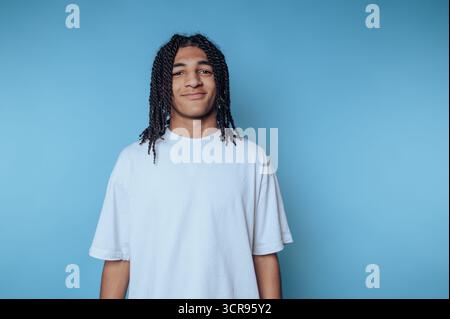 smiling young man stands warmly against a blue wall, embodying positivity and inviting energy Stock Photo
