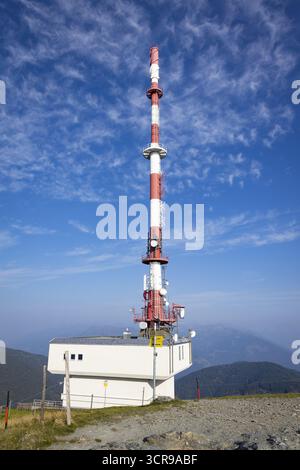 View of a tall, red and white communication tower rises against a clear blue sky dotted with fluffy clouds, Goldeck, Kärnten, Austria. Stock Photo