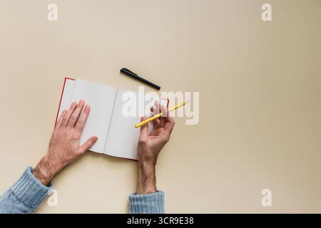 Top view of male hands holding pencil and open notebook with blank pages. Concept of bullet journal, creative writing, note taking, writer’s block Stock Photo