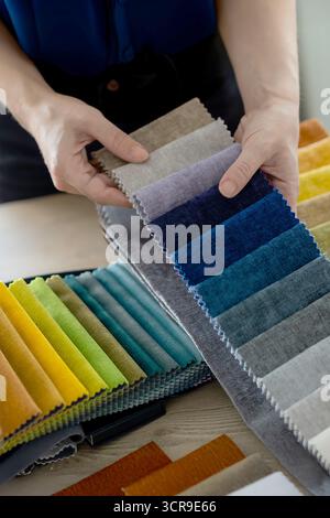 Female hands browsing fabric swatches in an upholstery showroom or artisan workshop. Concept of upholstery, home renovation, interior design Stock Photo