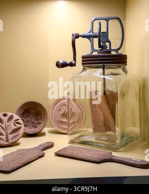 Vintage butter churn with wooden paddles surrounded by traditional wooden butter moulds in a yellow-lit display, uk Stock Photo