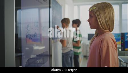 Close Up of Beautiful European Schoolgirl Working at Large Digital Screen During Lesson in Bright, Modern Classroom. AI Tools in Modern Education System. Concept of STEM Education. Static Shot. Stock Photo