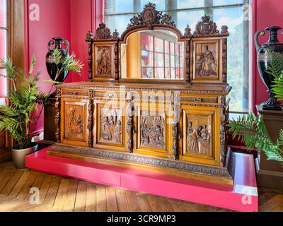 Elaborately carved wooden sideboard intricate figures & mirror in room  pink walls & decorative plants Bowes museum  Barnard Castle yorkshire dales Stock Photo