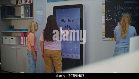 Students Interact With AI Mood Tracker in Modern Class. Girls Use AI Mood Tracker Interactive Digital Screen to Determine Emotional State. Using Technologies in Modern Schools For Emotional Learning. Stock Photo