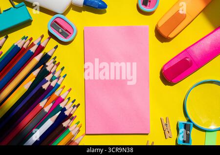 Flat lay of school supplies with pink sheet in center on yellow background. Creative back to school concept with copy space for text or design.  Stock Photo