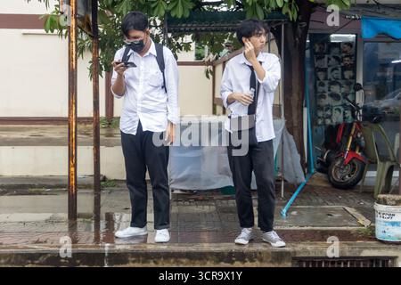BANGKOK, THAILAND, OCT 06 2024, Two young men waiting at a bus stop in a city area during rainy weather Stock Photo