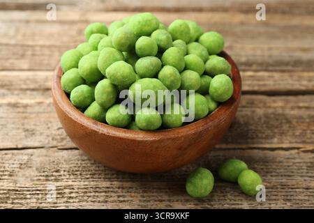 Delicious wasabi coated peanuts in bowl on wooden table, closeup Stock Photo