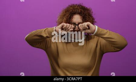 Woman rubbing eyes looking incredulous over bright pink wall wearing glasses brown sweater middle age brunette hispanic isolated setting conveying dis Stock Photo