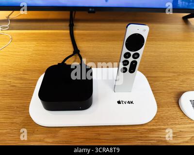 Manchester, UK - September 29, 2025: Compact media setup featuring Apple TV 4K and remote on a white dock beside a TV. Stock Photo