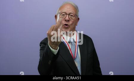 Senior man in suit with medal making gesture against purple background Stock Photo