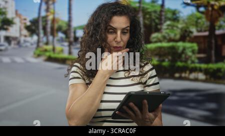 Woman on city street holding tablet with one hand and touching forehead with the other while staring at screen; surprise. Stock Photo