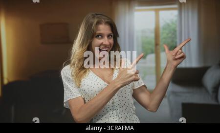 Woman points fingers to the right with both hands inside a building doorway, smiling and winking at camera; playful spontaneity. Stock Photo