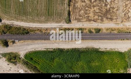 A railroad stretching between green fields and harvested lands. Agricultural and transportation infrastructure. Stock Photo