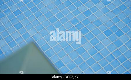 Outdoor sunny blue tiles background reflecting sunlight with blurred concrete at the corner creating a soothing visual with geometric patterns perfect Stock Photo