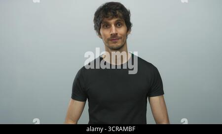 Man arms crossed in gray studio wearing casual black shirt and smirking gently; confidence strength poise. Stock Photo