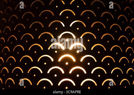 Artistic close-up of a glowing decorative lamp with geometric cut-out patterns, radiating a warm golden light. Great for backgrounds, interior design, Stock Photo