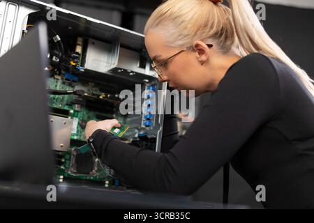 Female IT technician in her 20s, Caucasian, upgrading and troubleshooting a server inside a workstation Stock Photo