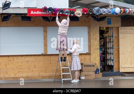 Eine Standlfrau mit ihrer Kollegin bringt ihre Ware Hüte von außen mit einer Stehleiter an der Andenken und Souvenir Bude an am Morgen vor Eröffnung des Oktoberfestes bei verregnetem Wetter Wolken Regen Schlechtwetter auf der Wiesn Oktoberfest in München / Datum: 30.09.2025 / *** A stand woman with her colleague brings her goods hats from the outside with a stepladder to the souvenir stall on the morning before the opening of the Oktoberfest in rainy weather Clouds Rain Bad weather at the Oktoberfest Oktoberfest in Munich Date 30 09 2025 Stock Photo