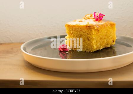 Close up of a piece of homemade apple pie with golden crust and juicy apple filling on a gray plate, decorated with small pink flowers. Concept of tra Stock Photo