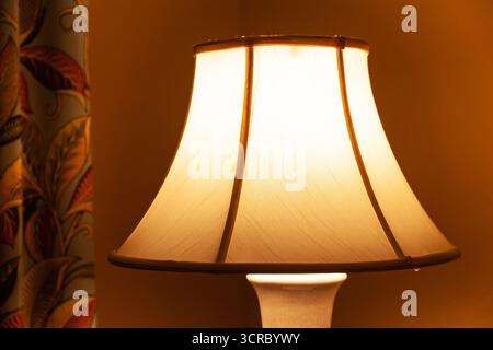 Cozy room nook with a curtain and a table lamp illuminating the area with soft yellow light, close up Stock Photo