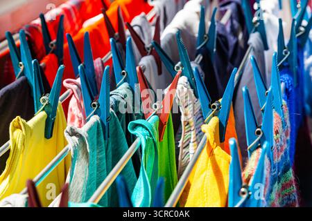 Multi-colored clothes hang attached to clothespins and dry after washing, close-up. Stock Photo
