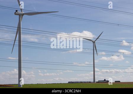 Wind turbines and electricity wires. Generation of electrical power and transportation of electrons by wires. Deliver generated power to substations. Stock Photo