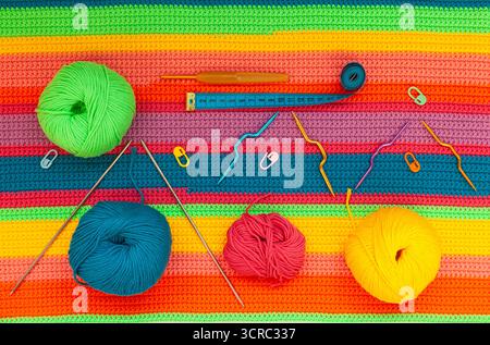 All for hand knitting. Knitted multi-colored handmade fabric with balls of multi-colored threads, pins, fabric measuring meter and various knitting ne Stock Photo