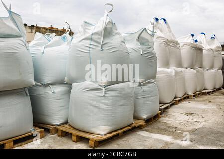 Large white industrial bags filled with construction materials are stacked on wooden pallets in an outdoor warehouse area, illustrating concepts of lo Stock Photo