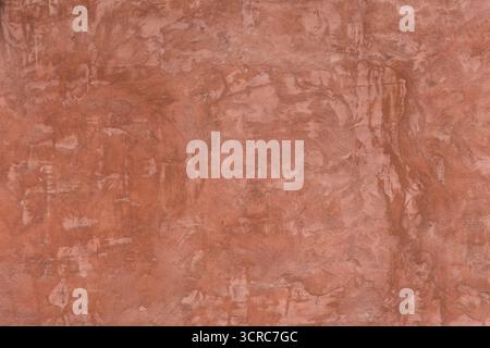 Close-up of a rustic red plaster wall showing natural imperfections, rough texture, and brush strokes Stock Photo