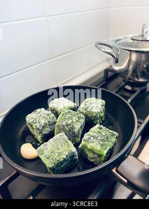 Frozen diced leaf spinach, a clove of garlic, and olive oil in a pan ready to be cooked. Healthy and vegetarian food. Overhead view. Stock Photo