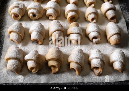 Croissants. Homemade small croissants sprinkled with icing sugar on a baking tray. Cornulețe, traditional Romanian dessert. Stock Photo