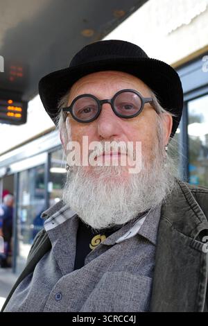 Elderly gentleman with bowler hat and round eyeglasses waits in the UK for the bus Stock Photo